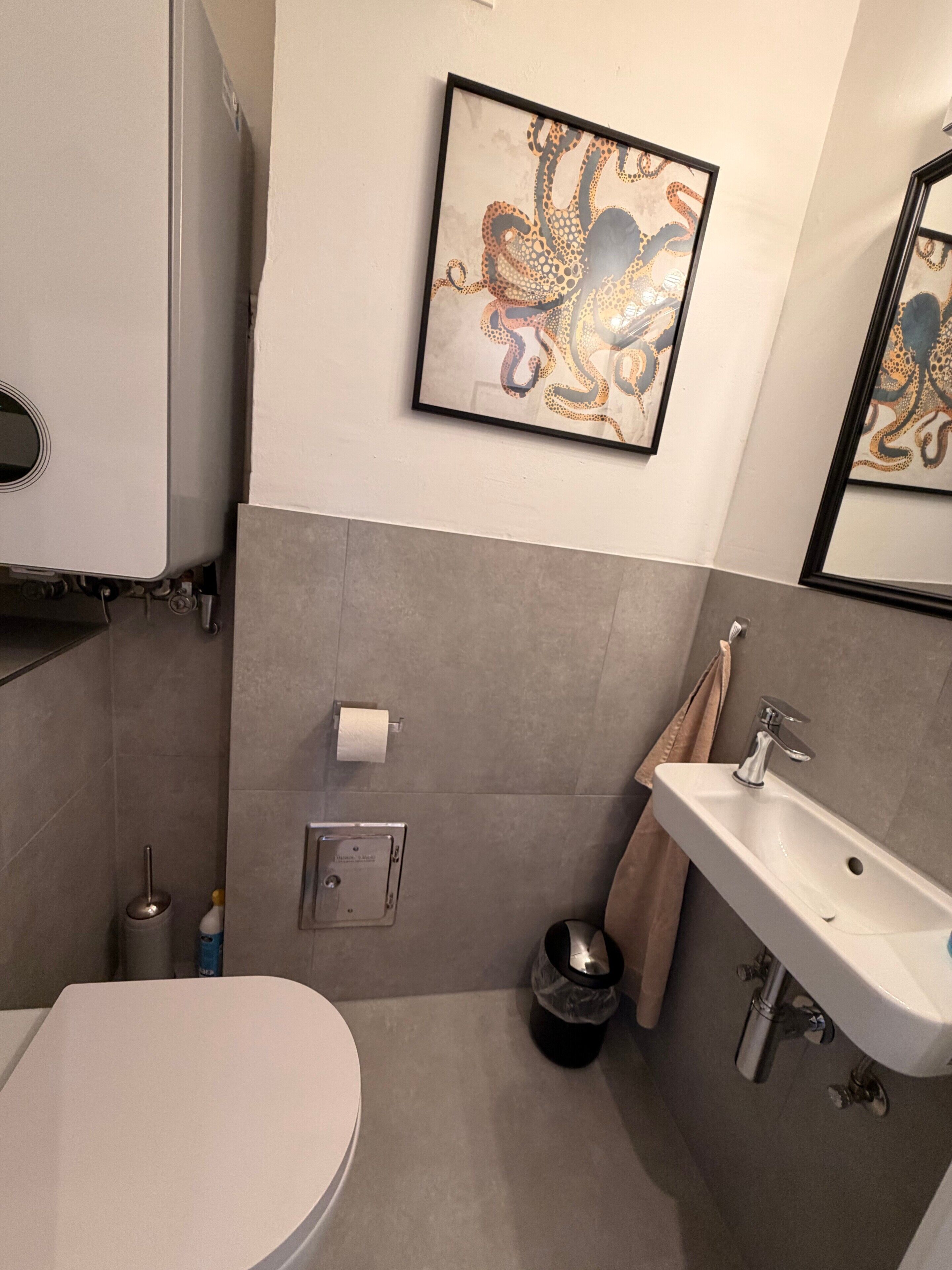 Et moderne badeværelse med en hvid vask, et spejl, et håndklædestativ og en toiletpapirholder.