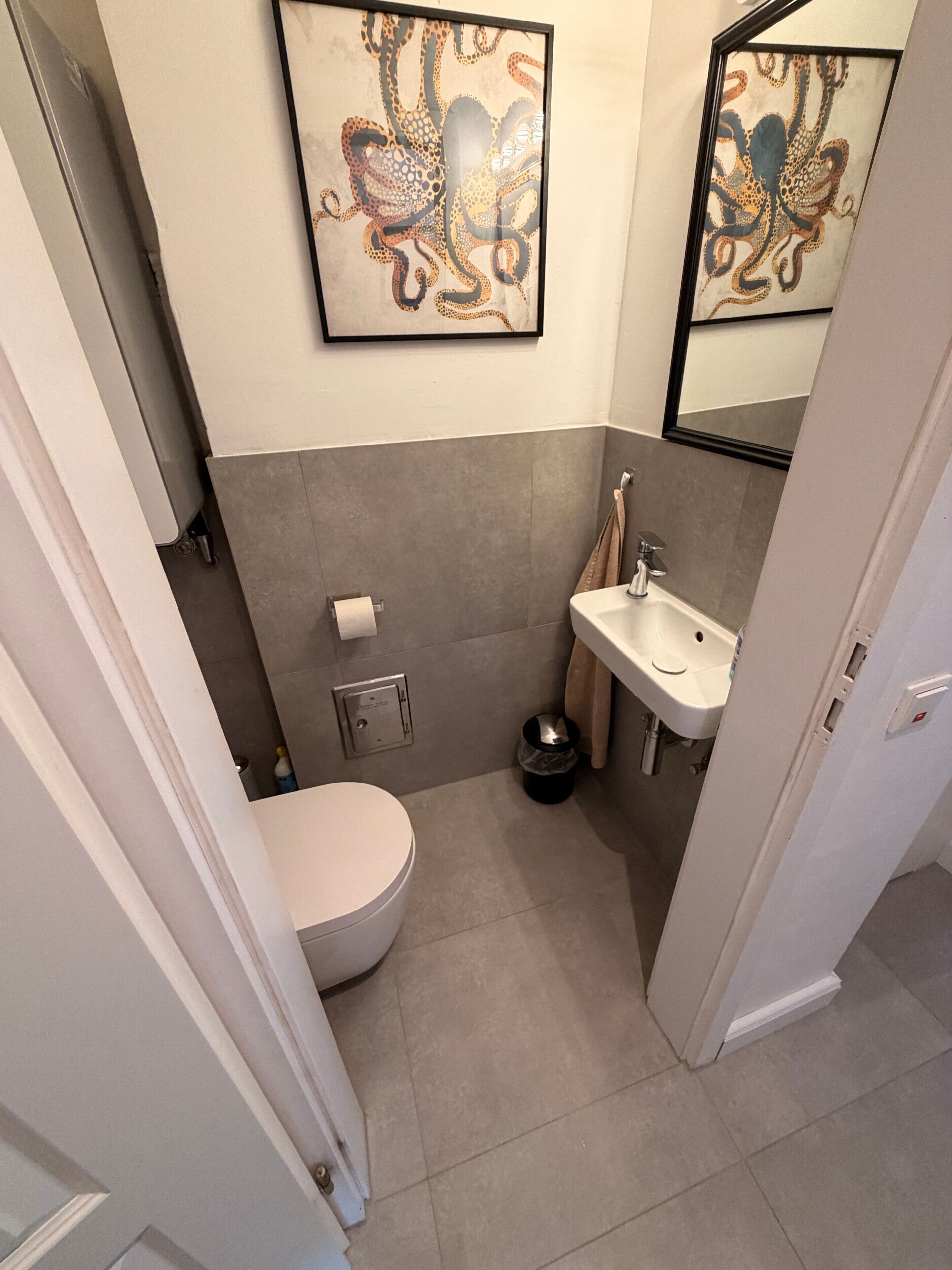 Un baño pequeño con inodoro, lavamanos y una obra de arte enmarcada en la pared.