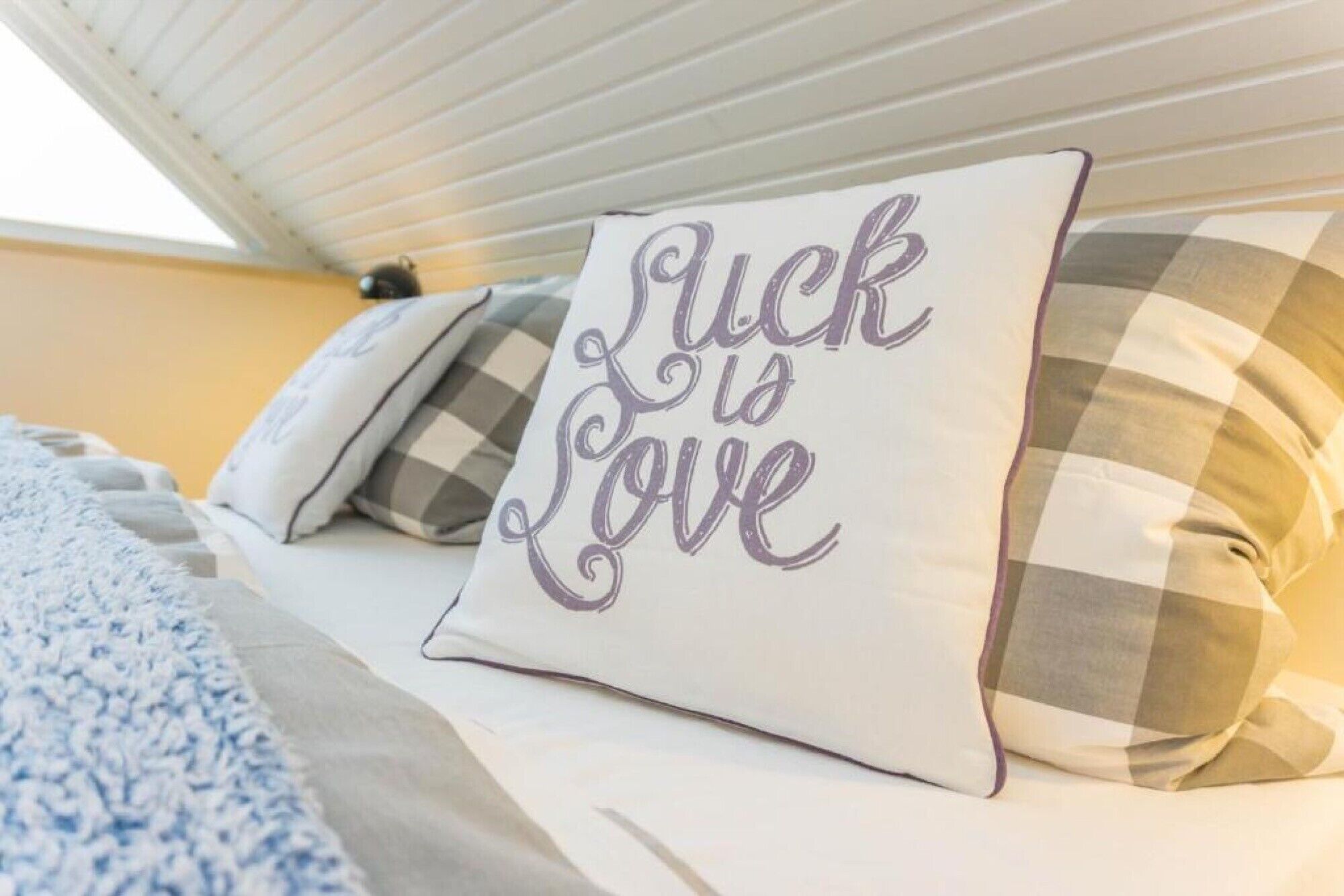 En seng med en pude, der siger 'Luck is Love', og en pude med tern.