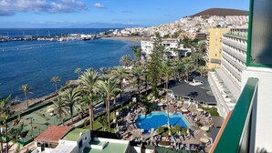 A coastal hotel with a swimming pool, palm trees, and a view of the sea and port. - Ocean View 2 (Los Cristianos)