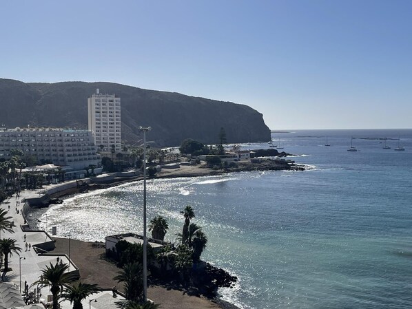 A coastal hotel with a beachfront view, a tall building in the background, and several boats in the water. - Ocean View 2 (Los Cristianos)