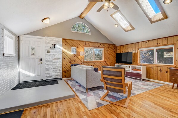 A cozy attic bedroom with a loft bed, a sofa, a TV, and a wooden ceiling.