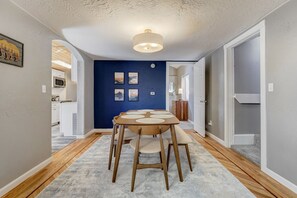 A dining area with a wooden table and chairs, a blue accent wall, and a ceiling light fixture.