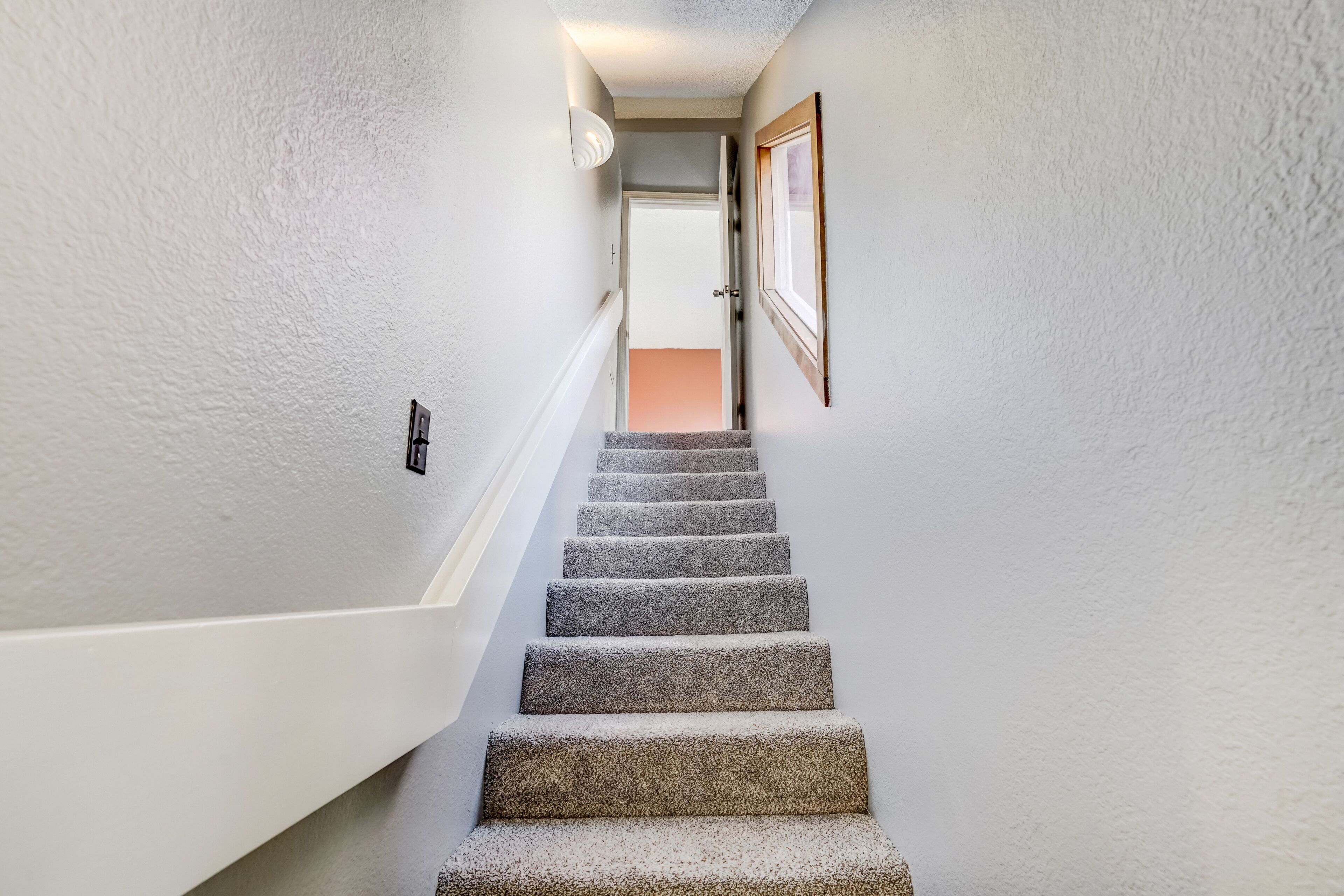 Un escalier dont les marches sont recouvertes de moquette, menant à une porte située en haut.