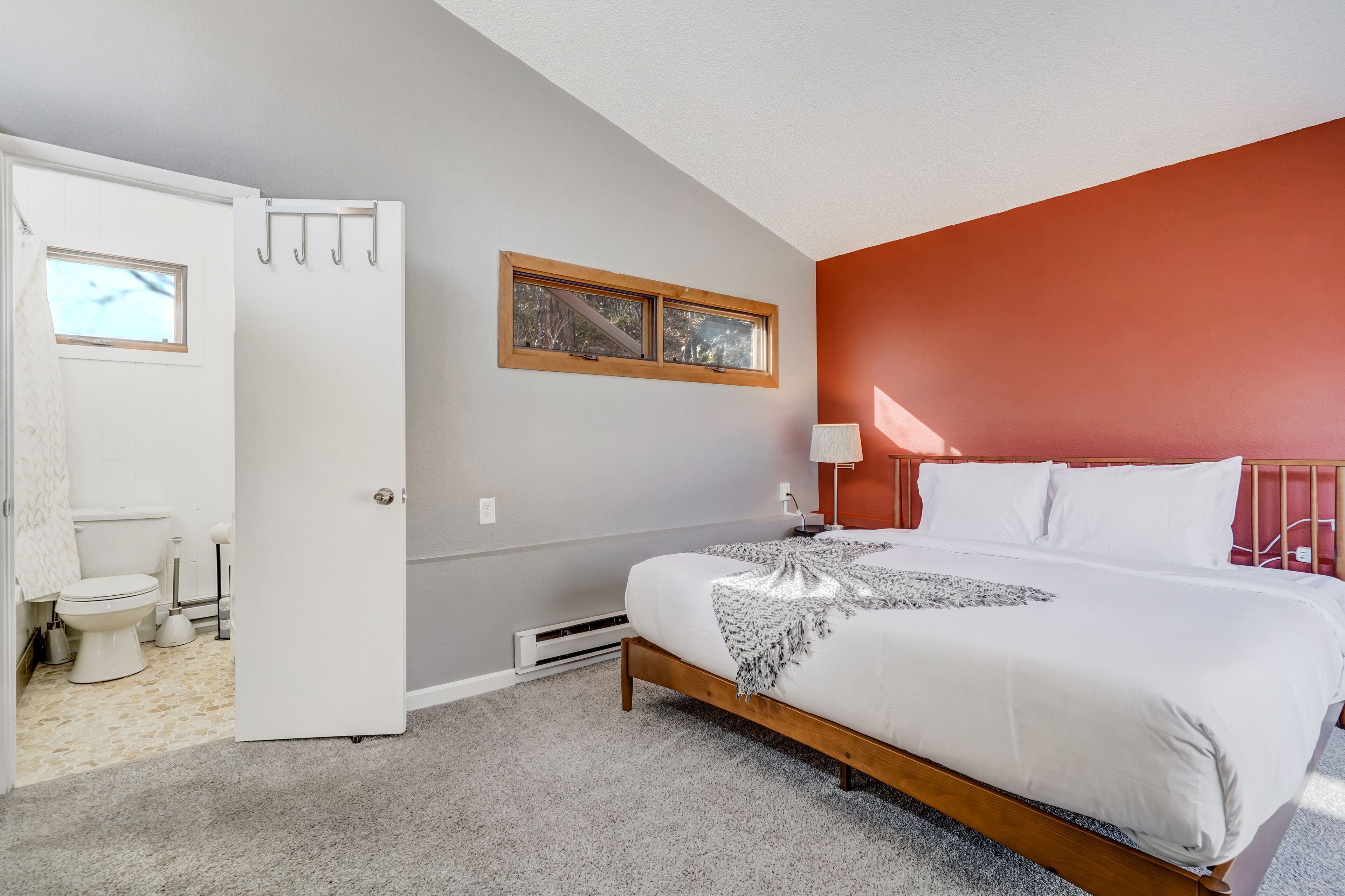 A bedroom with a bed, a window, a door, and a bathroom visible through an open door.