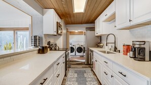 A modern kitchen with white cabinets, a skylight, a washing machine, and a coffee maker.