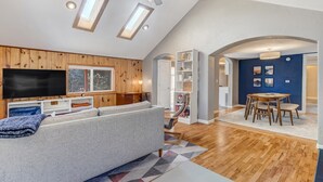 A modern loft-style living space with a large TV, a sofa, a dining area, and a skylight.