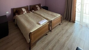 Cama doble con estructura de madera y dos almohadas, una mesita de noche y una ventana con cortinas.
