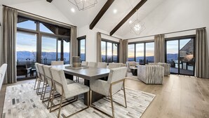 A spacious dining area with a large table and chairs, large windows with mountain views, and modern lighting fixtures.