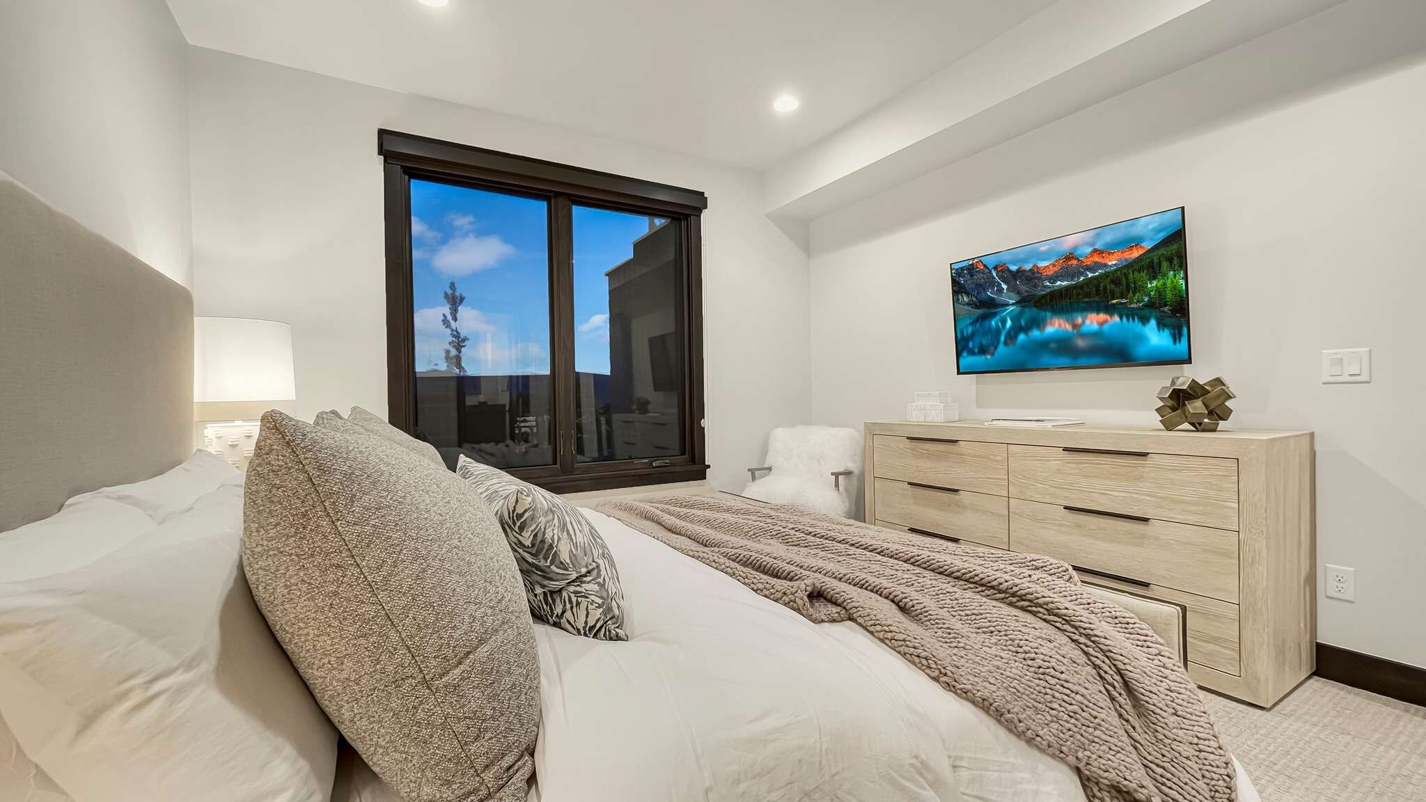 Une chambre à coucher avec un lit, une commode, un téléviseur et une fenêtre donnant sur un beau paysage.