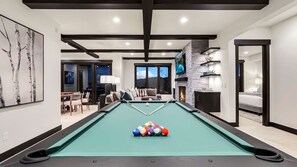 A pool table with a fire feature, a sofa, and a television in a modern living room. - Elegant Mountain Abode w/ 4 King Suites•Hot Tub•Billiards•Sweeping 180° Views (Park City)