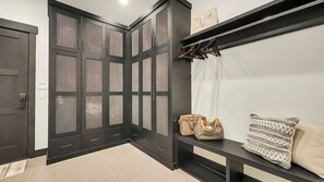Una habitación moderna con un armario de color oscuro, un banco con maletas y un perchero.