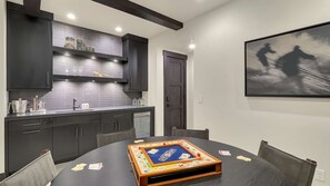 A modern kitchen with dark cabinetry, a built-in oven, and a dining table set for a board game. - Elegant Mountain Abode w/ 4 King Suites•Hot Tub•Billiards•Sweeping 180° Views (Park City)