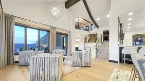 A spacious living area with a large window offering a view of the outdoors, a staircase leading to an upper level, and a modern chandelier.