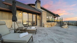 A modern outdoor patio with lounge chairs, a table, and a stone fireplace.