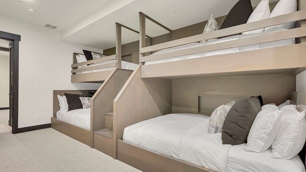 Une chambre avec des lits superposés, un escalier menant au lit supérieur, du linge de lit blanc et une porte sur le côté gauche.