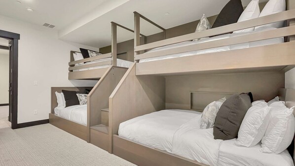 A bunk bed room with a staircase leading to the upper bunk, white bedding, and a door to the left.