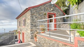 A stone building with a red roof, a satellite dish, and a small balcony with a railing. - Ocean View Cottage, a Home in Madeira (Fajã da Ovelha)