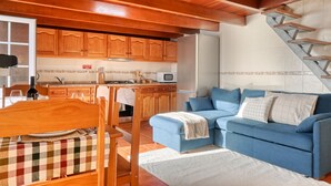 A compact living space with a kitchenette, a dining area, and a blue sofa. - Ocean View Cottage, a Home in Madeira (Fajã da Ovelha)