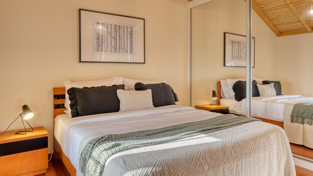 A bedroom with a large bed, a bedside table with a lamp, a mirror, and framed artwork on the wall. - Ocean View Cottage, a Home in Madeira (Fajã da Ovelha)