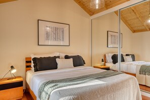 Un dormitorio con una cama grande, una mesita de noche con lámpara, un espejo y cuadros en la pared.
