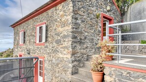 A stone building with red-framed windows and a metal railing. - Ocean View Cottage, a Home in Madeira (Fajã da Ovelha)