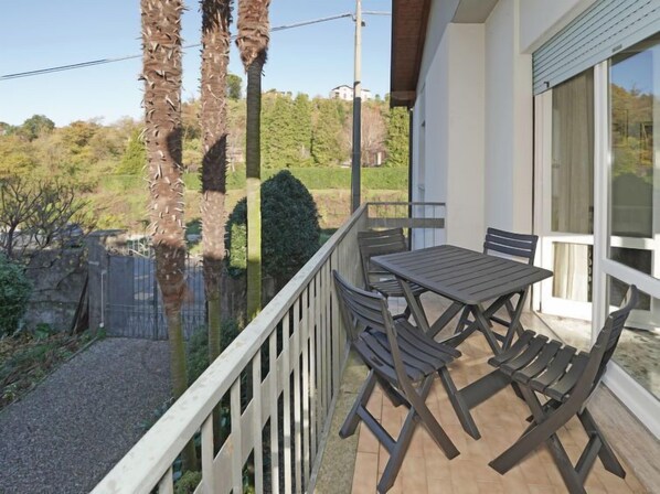 A balcony with a table and chairs, overlooking a garden and a forested area.