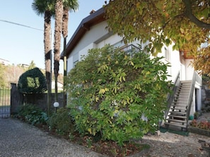 A building with a staircase leading to a second floor, surrounded by various plants and a palm tree.