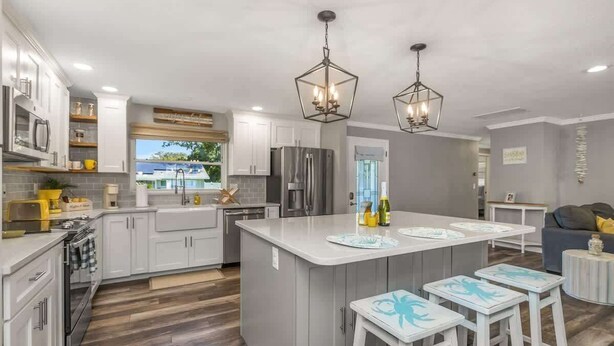 A modern kitchen with white cabinets, a central island, bar stools, and a dining area.