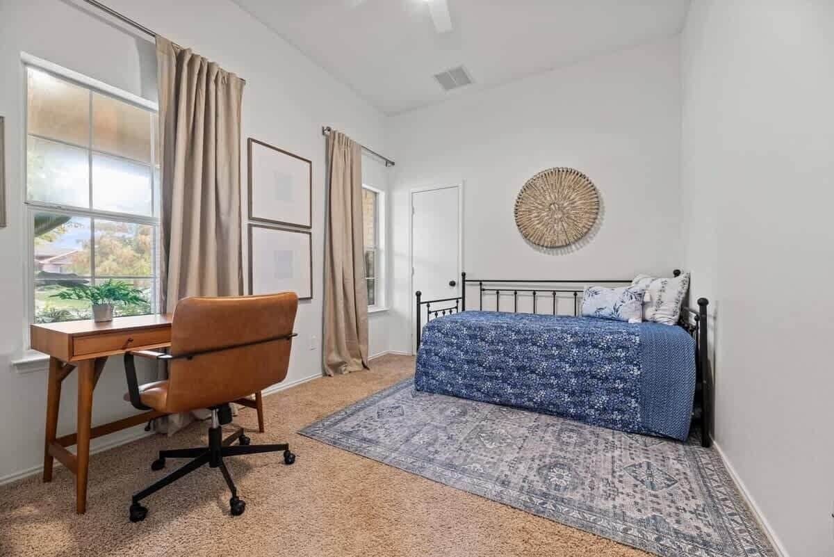 Quarto com cama, escrivaninha, cadeira, janela com cortinas e um ornamento na parede.