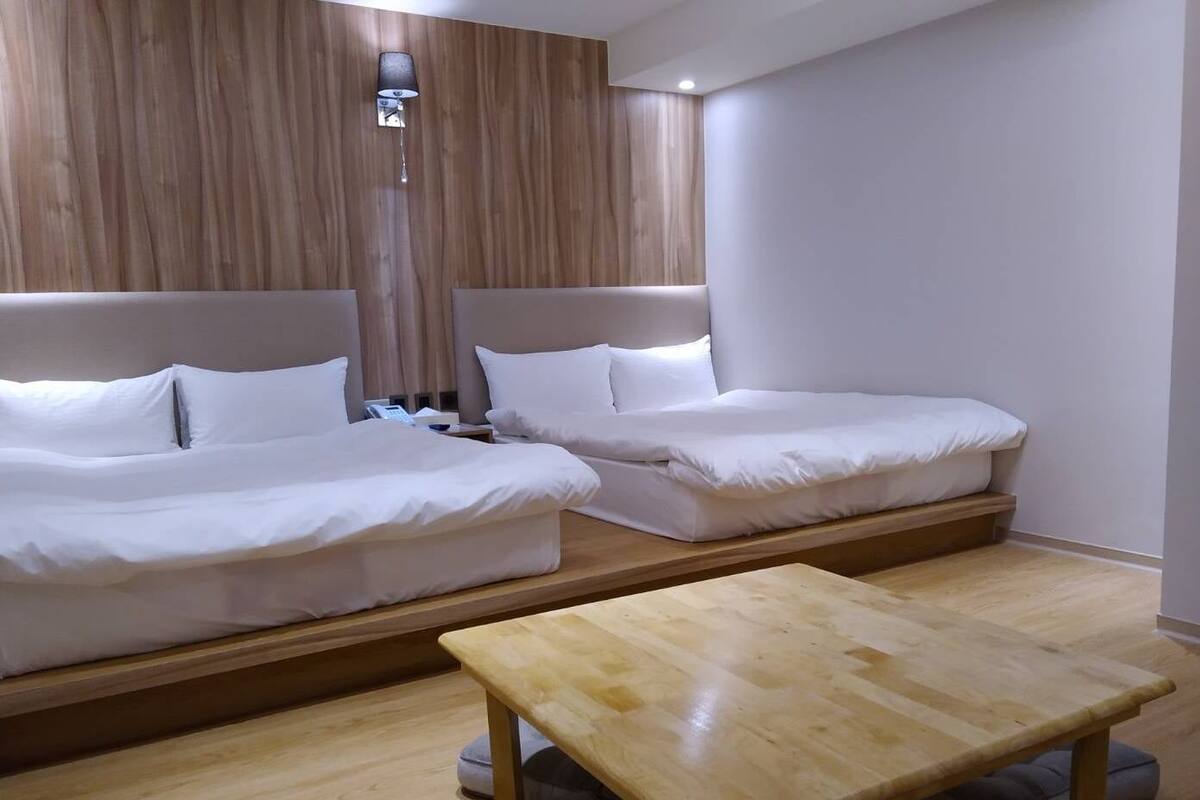 A hotel room with two beds, a wooden table, and a wall-mounted lamp.