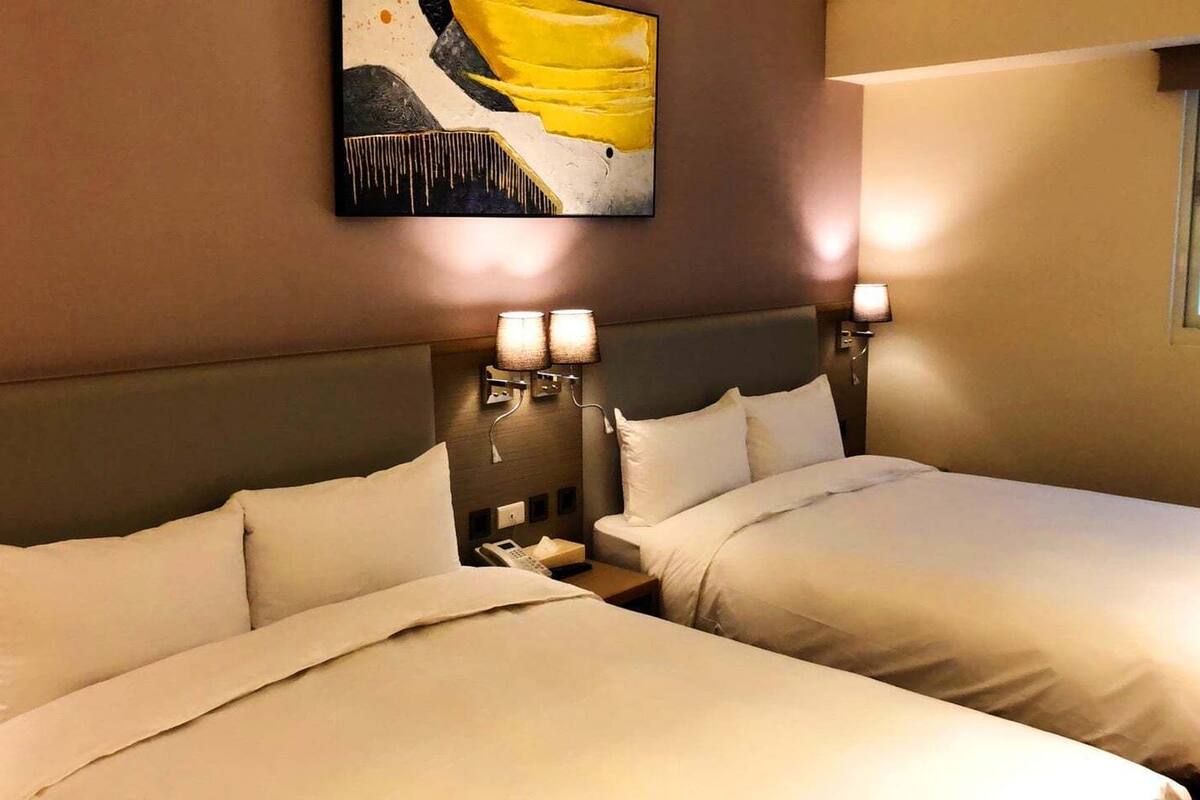 A hotel room with two beds, a painting on the wall, and bedside lamps.