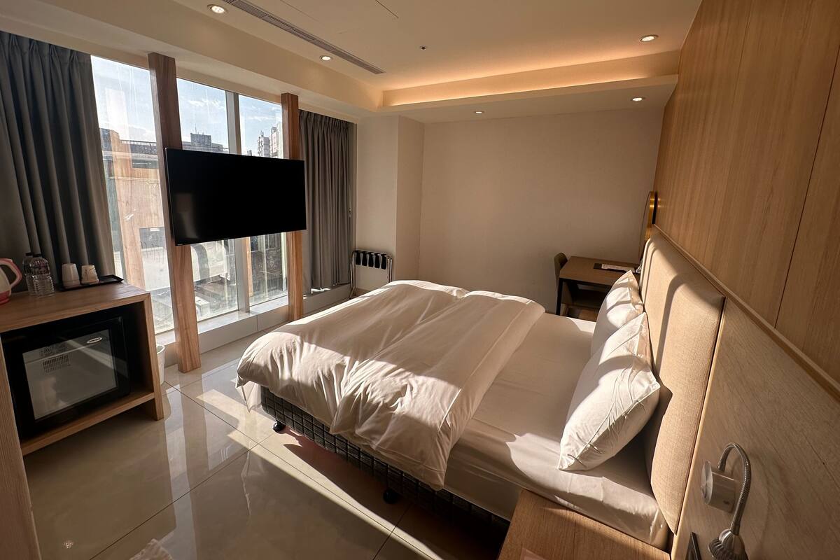 A modern hotel room with a large bed, a flat-screen TV, a desk, and a view of the city.
