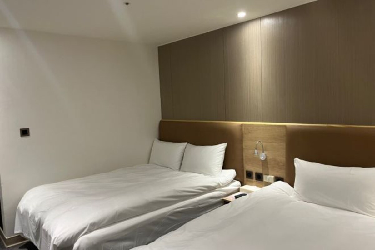 Una habitación de hotel con dos camas individuales, un cabecero de madera y una mesita de noche con lámpara.