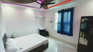 Une chambre à coucher comprenant un lit, une armoire, un ventilateur de plafond, une fenêtre avec des rideaux et un miroir.