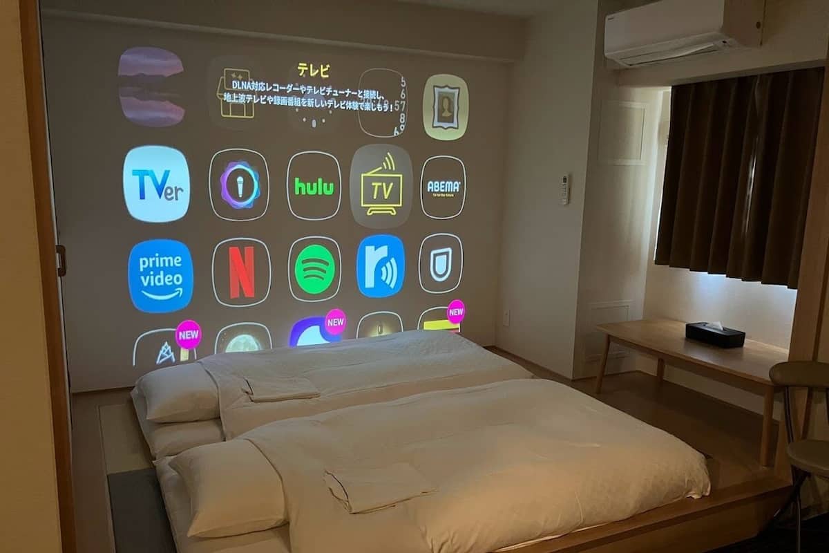 Une chambre d’hôtel équipée d’un lit, d’un bureau et d’un écran fixé au mur affichant les icônes de différents services de diffusion en continu.