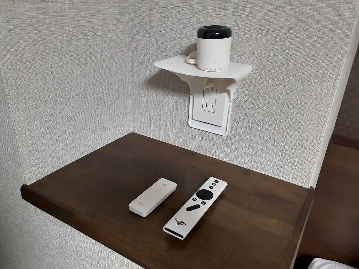 A small table with a remote control and a white device on it, and a wall-mounted device above.