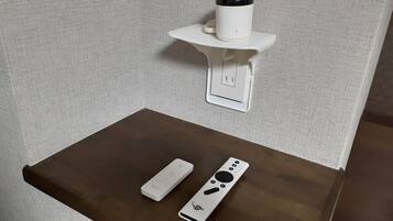 A small table with a remote control and a white device on it, and a wall-mounted device above.