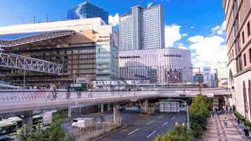 A modern urban street scene with a pedestrian bridge, a tram, and various buildings including a hotel.
