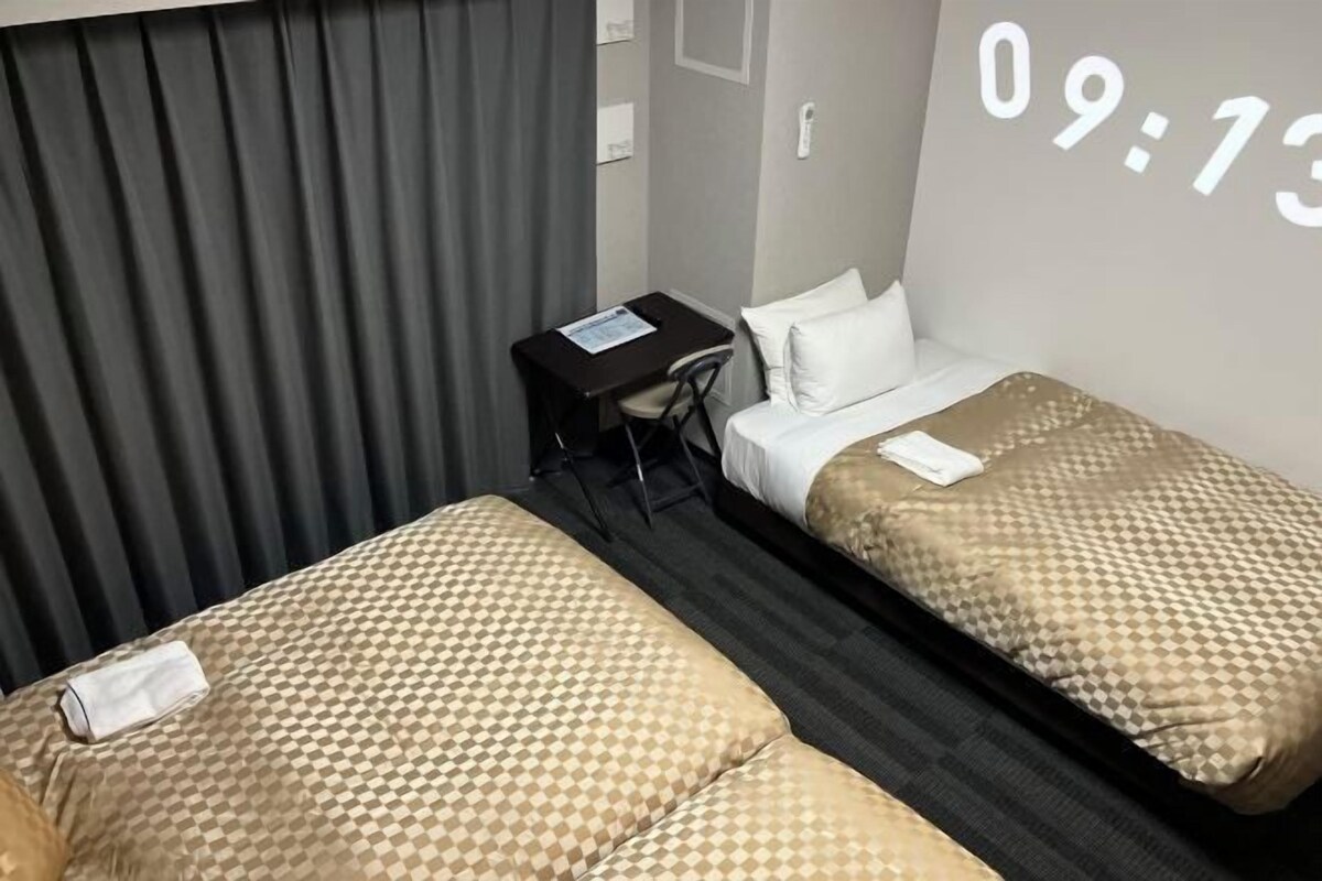 Habitación de hotel con dos camas, un escritorio y un televisor que muestra la hora.
