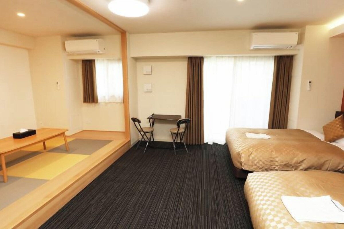 Habitación de hotel con cama, escritorio, dos sillas y un equipo de aire acondicionado.