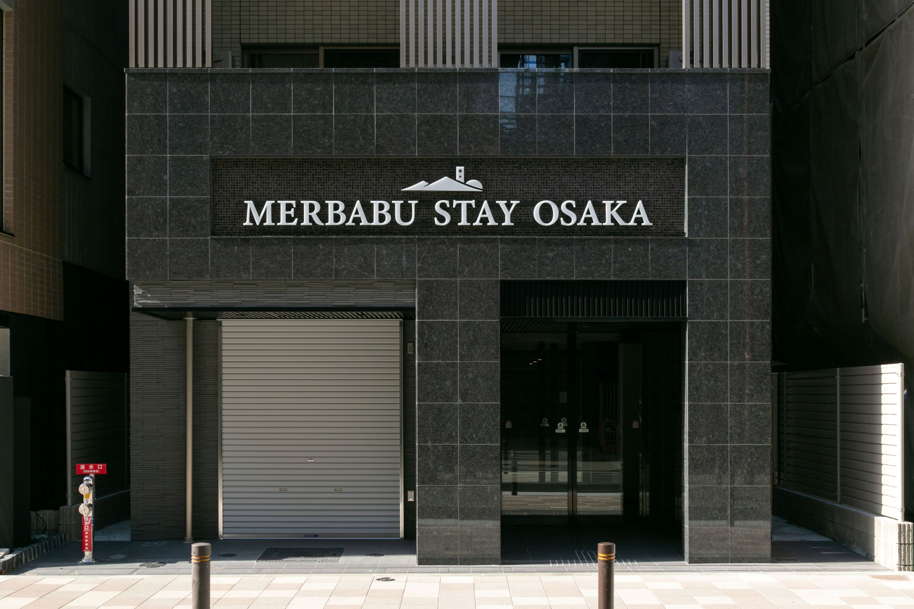 Het uiterlijk van het Merbabu Stay Osaka gebouw, met een gesloten luik en een bord erboven.