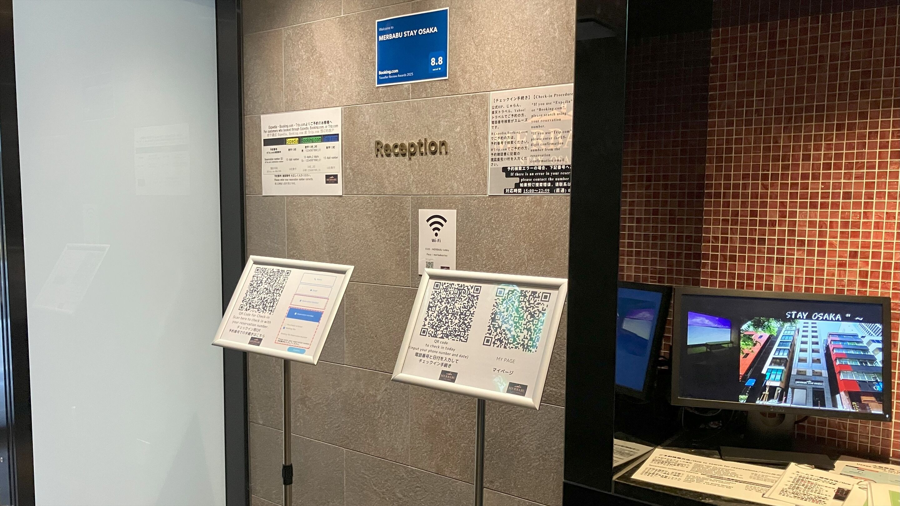 A reception area with a monitor displaying a cityscape, a Wi-Fi sign, and several informational posters.