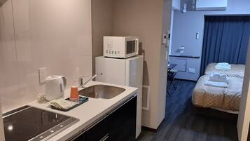 Una habitación de hotel compacta con kitchenette, una cama y una pequeña zona de estar.