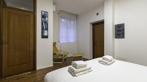 A hotel room with a bed, two chairs, a window with curtains, and a door. - Italianway Easy - Piceno 44 (Milan)