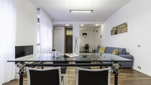 A modern dining area with a glass table, black chairs, and a sofa in the background. - Italianway Easy - Piceno 44 (Milan)