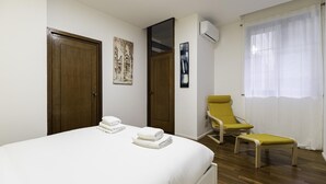 A bedroom with a bed, two doors, a chair, a bench, a wall-mounted air conditioner, and a window with curtains. - Italianway Easy - Piceno 44 (Milan)