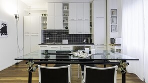 A modern kitchen with white cabinets, a black tiled backsplash, and a glass dining table with two chairs. - Italianway Easy - Piceno 44 (Milan)