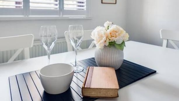 A dining table with a white bowl, two wine glasses, a book, and a vase with flowers. - Cosy 2-bedroom Haven in Picturesque Headington (Oxford)