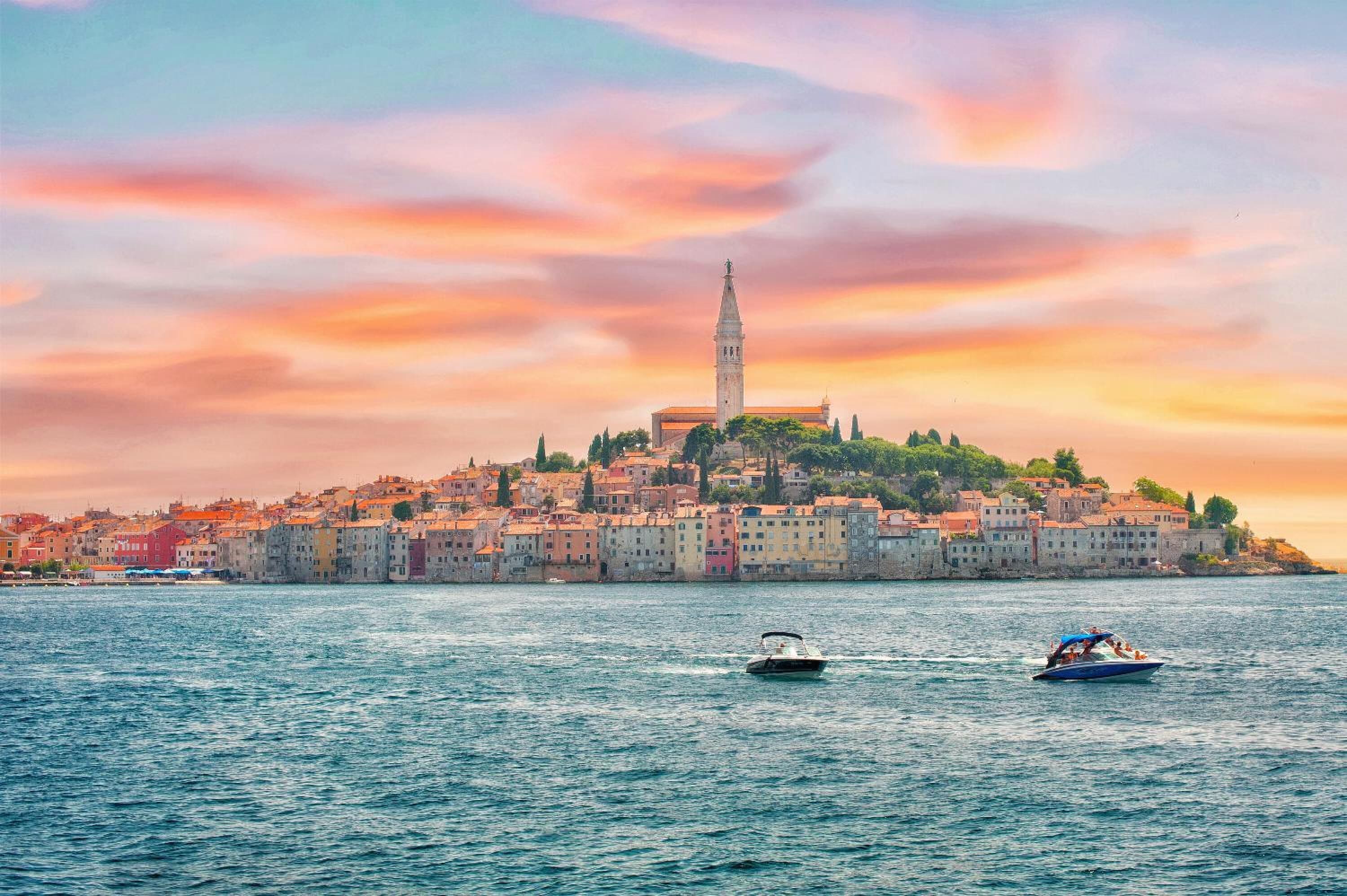 Paisagem costeira com uma torre imponente, barcos na água e edifícios coloridos.